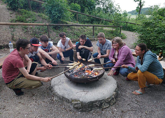 Gruppe die um ein Lagerfeuer Stockbrot grillen